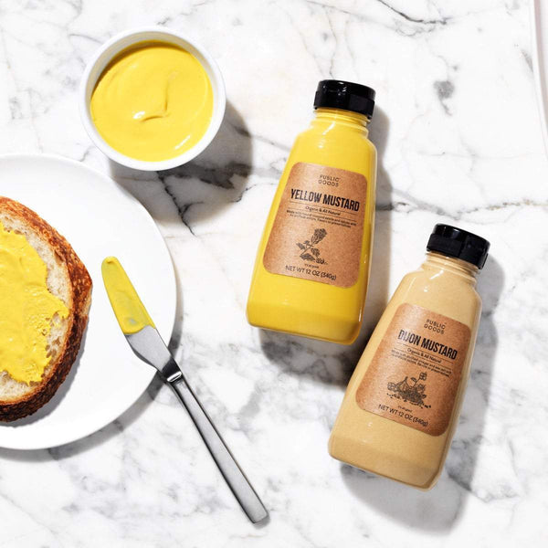 white bread with mustard on plate, bottle of public goods yellow mustard, bottle of public goods dijon mustard, side dish with yellow mustard