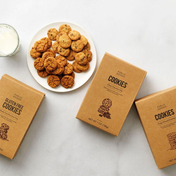 three boxes of public goods cookies, plate of crispy chocolate chip and oatmeal cookies, glass of milk