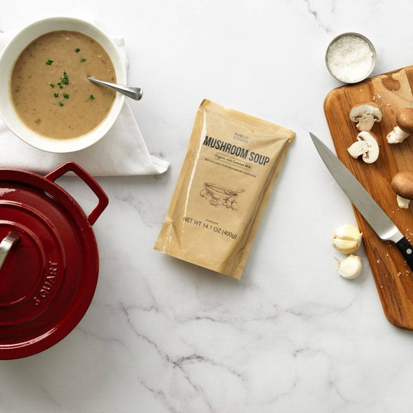 bag of mushroom soup, bowl of mushroom soup, chopped mushrooms on wooden cutting board, salt, garlic cloves, red cooking pot with lid