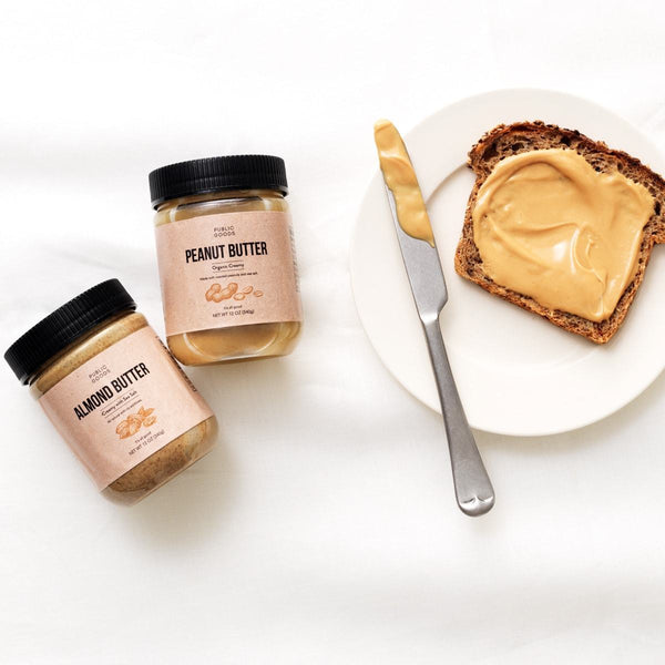 jar of almond butter, jar of peanut butter, toast with peanut butter on plate, knife smeared with peanut butter
